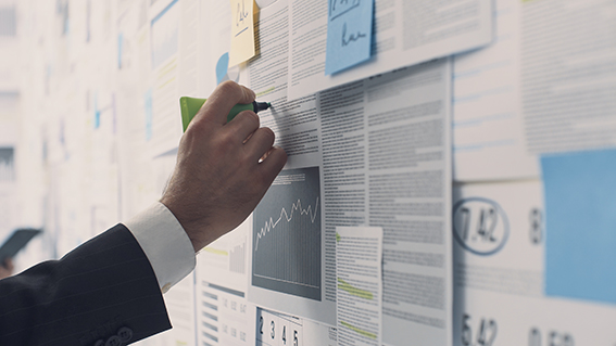 Businessman analyzing a wall with many financial charts and reports, he is underlining text with a marker